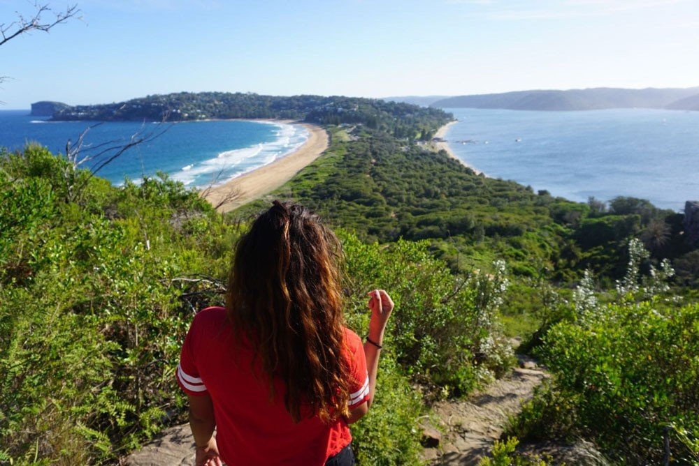 Experiencia en Australia chica morena con el pelo rizado de espaldas observando un paisaje de montaña y mar.