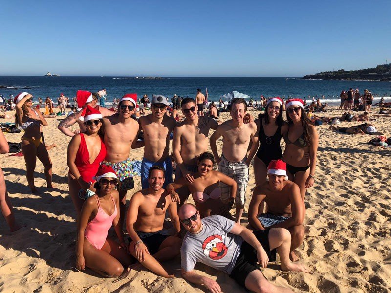 Navidad Australia grupo de amigos posando en la arena en bikini y gorros de navidad en la playa de Sydney con el mar de fondo