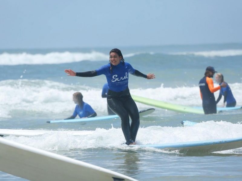 Surf Australia chica morena en una tabla de surf en la playa de Sydney con gente detrás que también hace surf