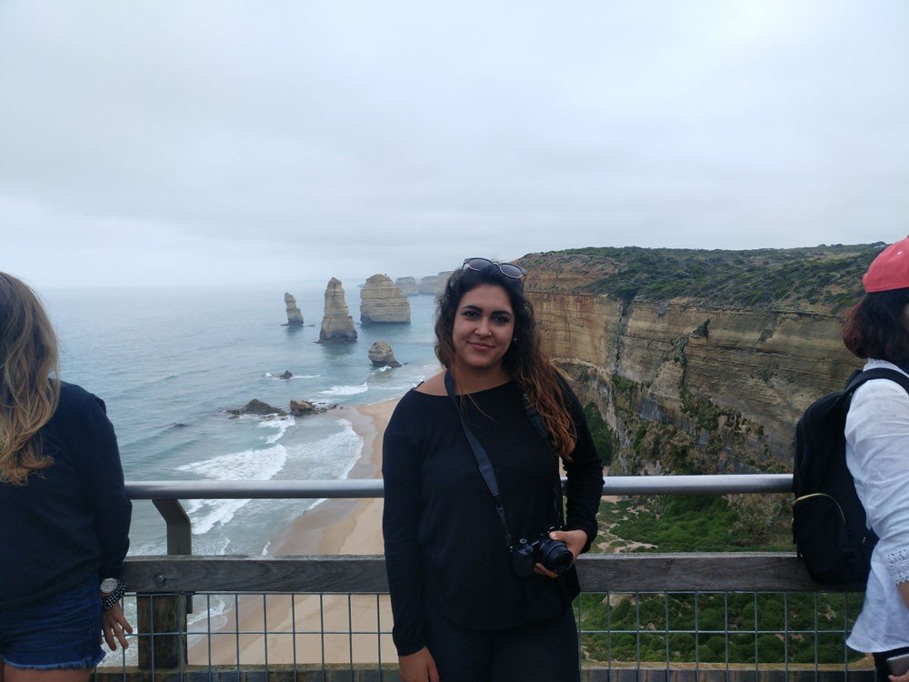 Vivir en Sydney chica morena vestida de negro y posando delante de los 12 apóstoles de Melbourne